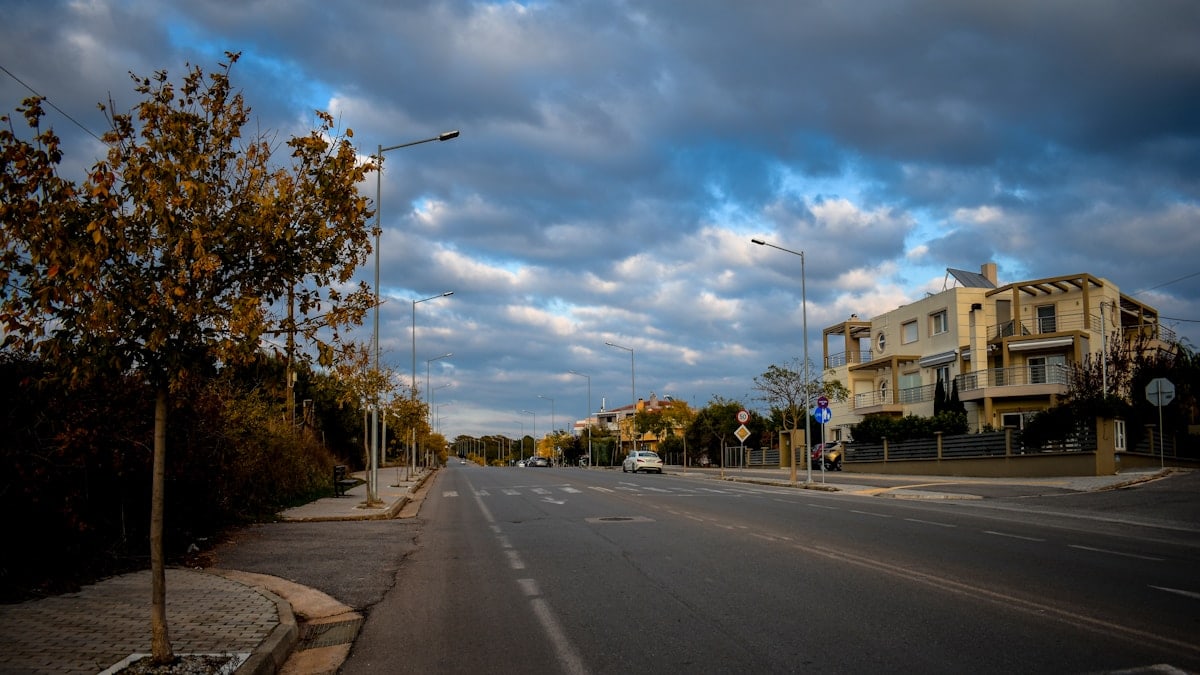 Empty road with buildings and trees under cloudy sky